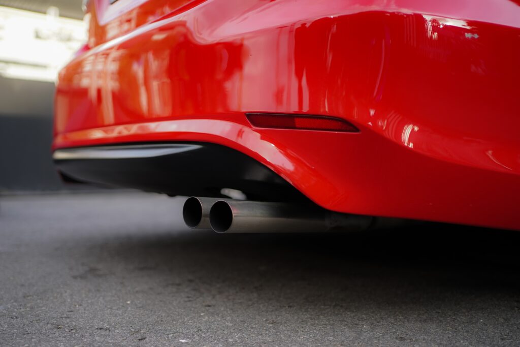 Rear end of Red sports car on pavement with two exhaust pipes.