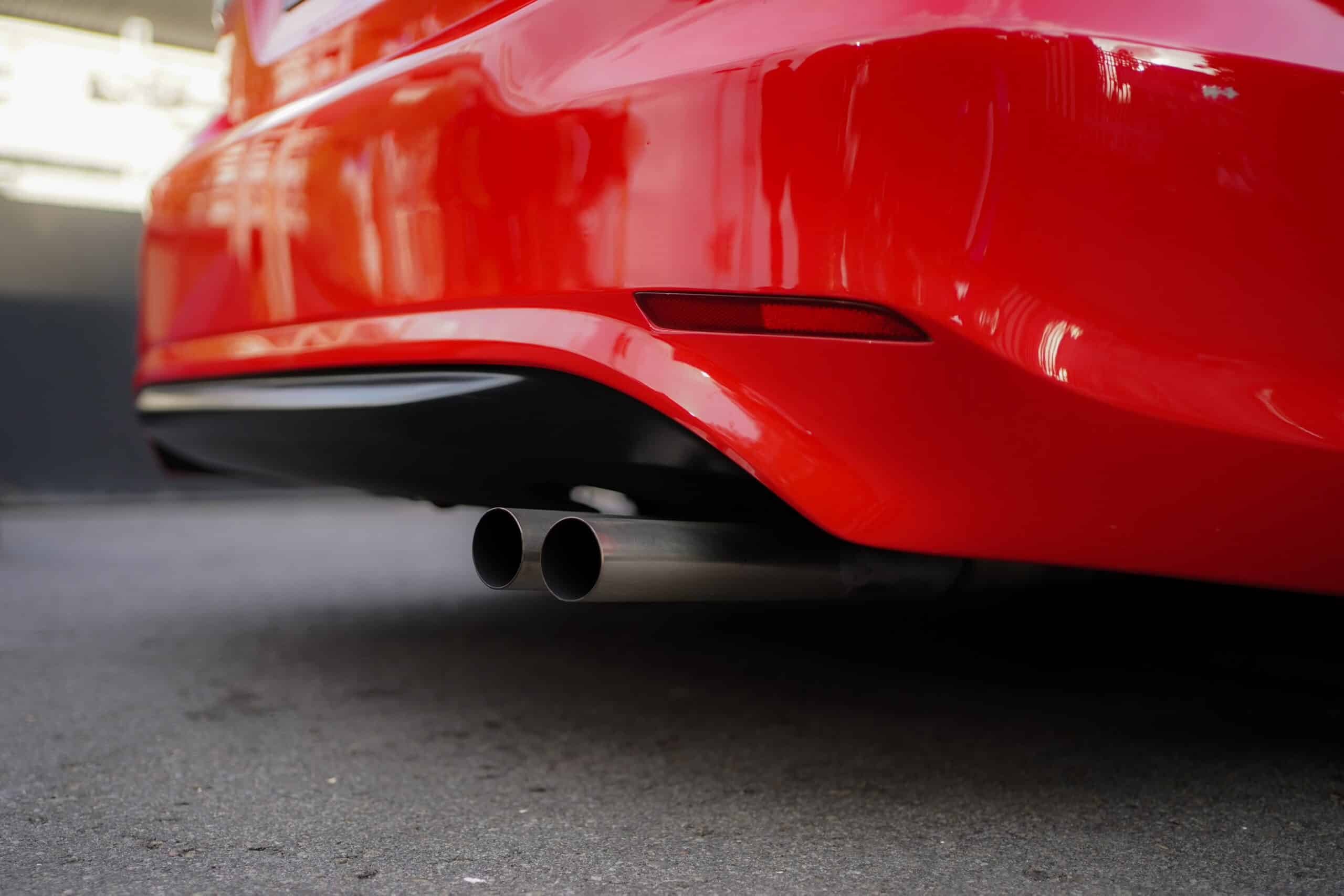 Rear end of Red sports car on pavement with two exhaust pipes.